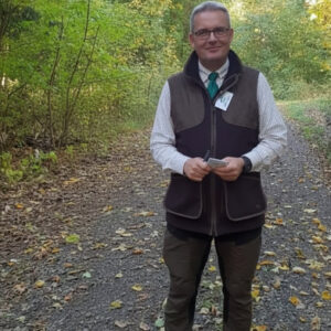 Mann im Wald bei Hunde-Event, trägt Jacke und Brille, lächelt.